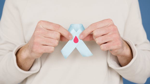 Close-up of a person holding a blue awareness ribbon featuring a red blood drop symbol.